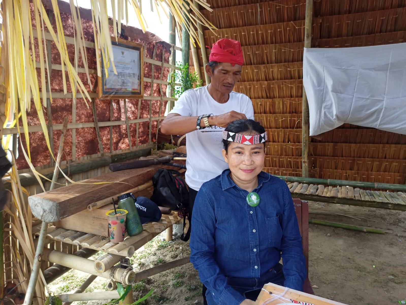 Safrudin warga Desa Mataue, Kecamatan Kulawi, Kabupaten Sigi, sedang memakaikan tali enu kepada salah seorang pengunjung Festival Lestari Kabupaten Sigi, Sabtu (24/6). (Foto: Irma/Media Alkhairaat)